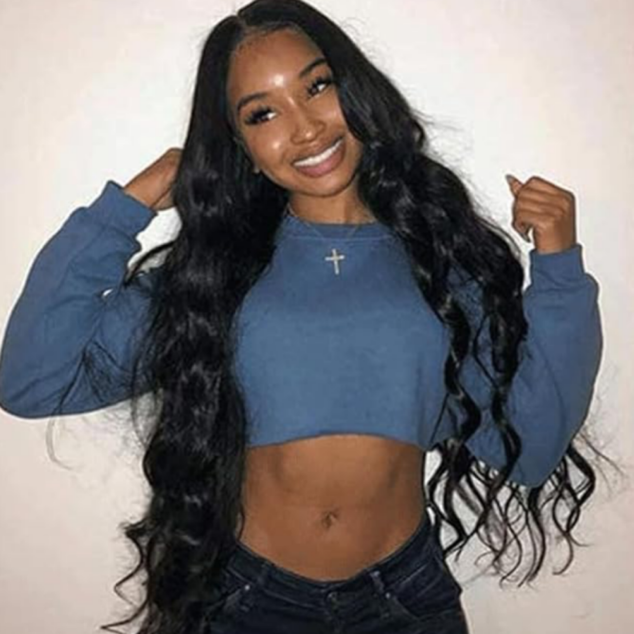 pretty woman wearing 3 bundles of virgin Brazilian  body wave in the lengths 26"28" and 30 inches and she's wearing a light blue shirt standing Infront of a white background