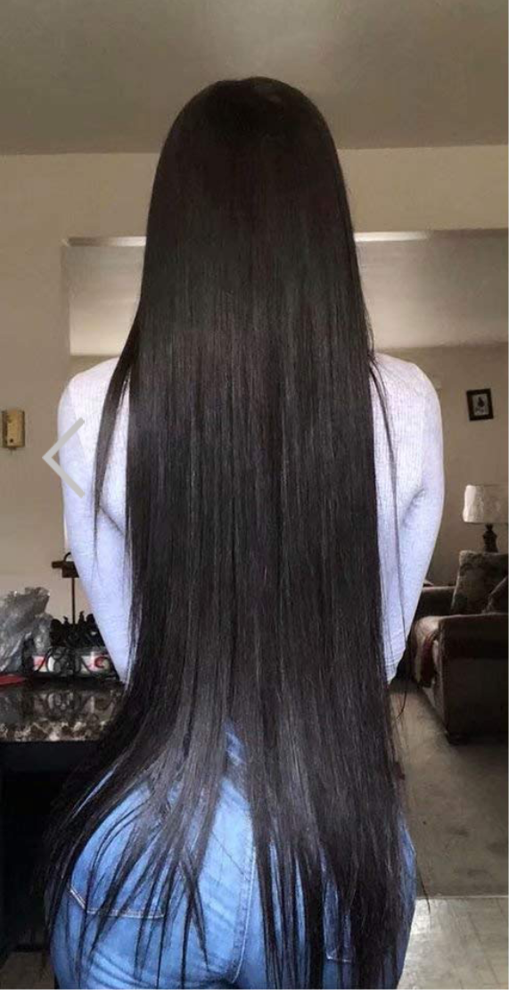 woman wearing 3 bundles of 30 inch bone straight virgin Brazilian hair with her back turned to the camera wearing a white long sleeve shirt with a living room with couches in the background